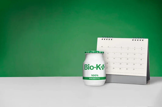 Bio-K+ probiotic bottle beside a desk calendar on green background