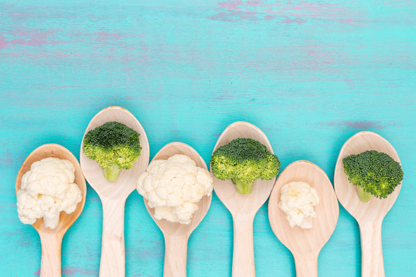 Top view of fresh cauliflower and broccoli with wooden spoons on a blue background.