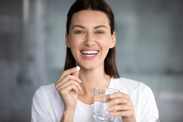 Woman smiling while holding a probiotic capsule and a glass of water