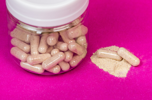Open capsules with powder spilled beside a jar of probiotic capsules on a pink background