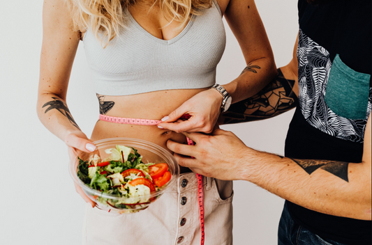 A woman holding a salad bowl while a measuring tape is wrapped around her waist