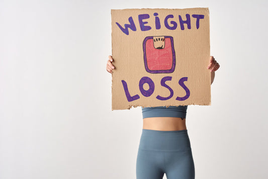 Woman holding cardboard sign that says "weight loss" with hand-drawn scale illustration