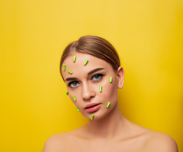 	Probiotics for clear skin concept: woman's face with green capsules placed on it against a yellow background