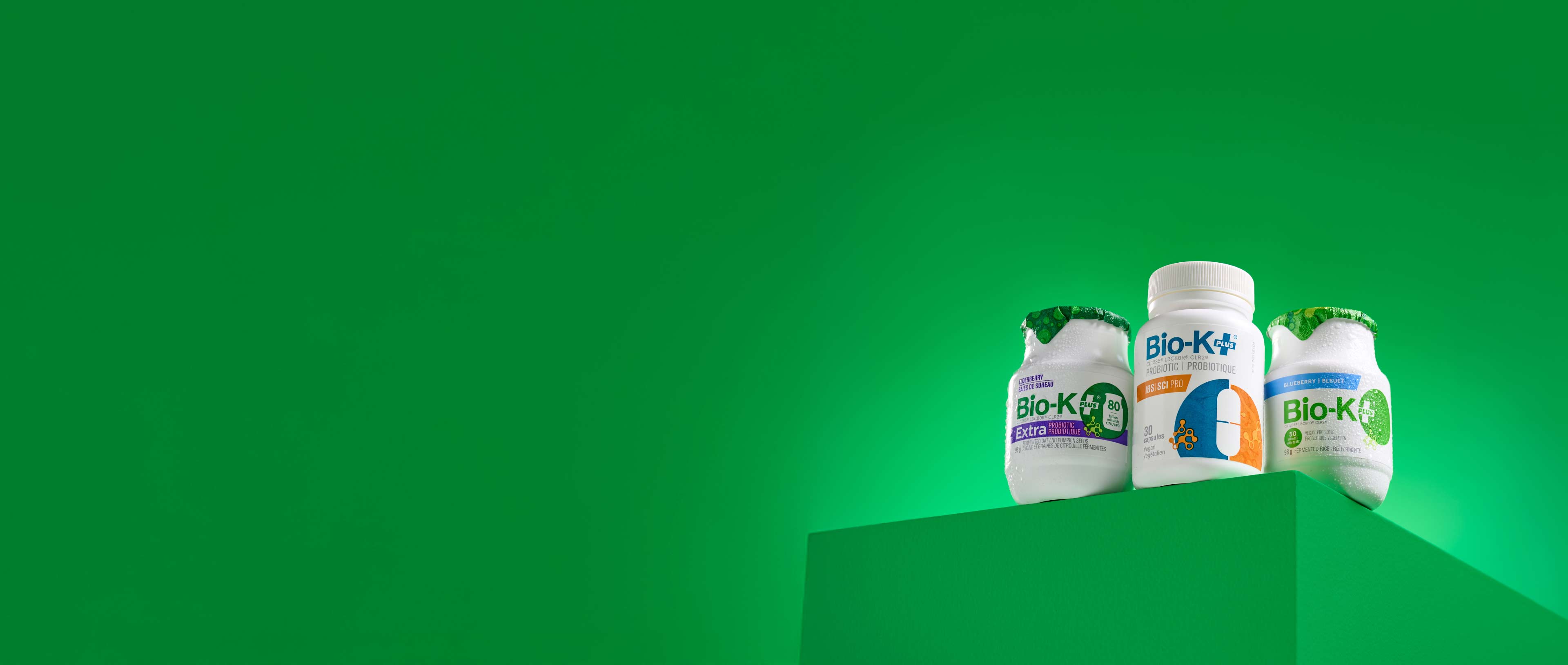 Three Bio-K+ supplement bottles on a green background