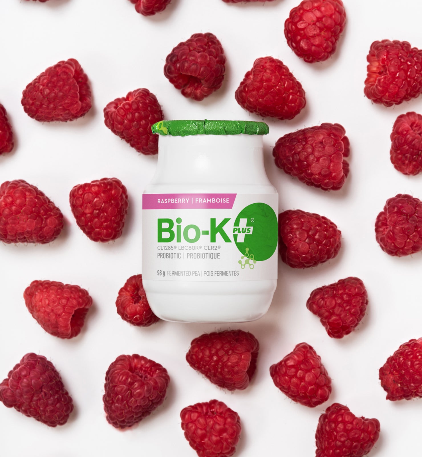 Bottle of Drinkable Vegan Probiotics - Fermeted pea base - Rasberry Flavour - on a background of real rasberries